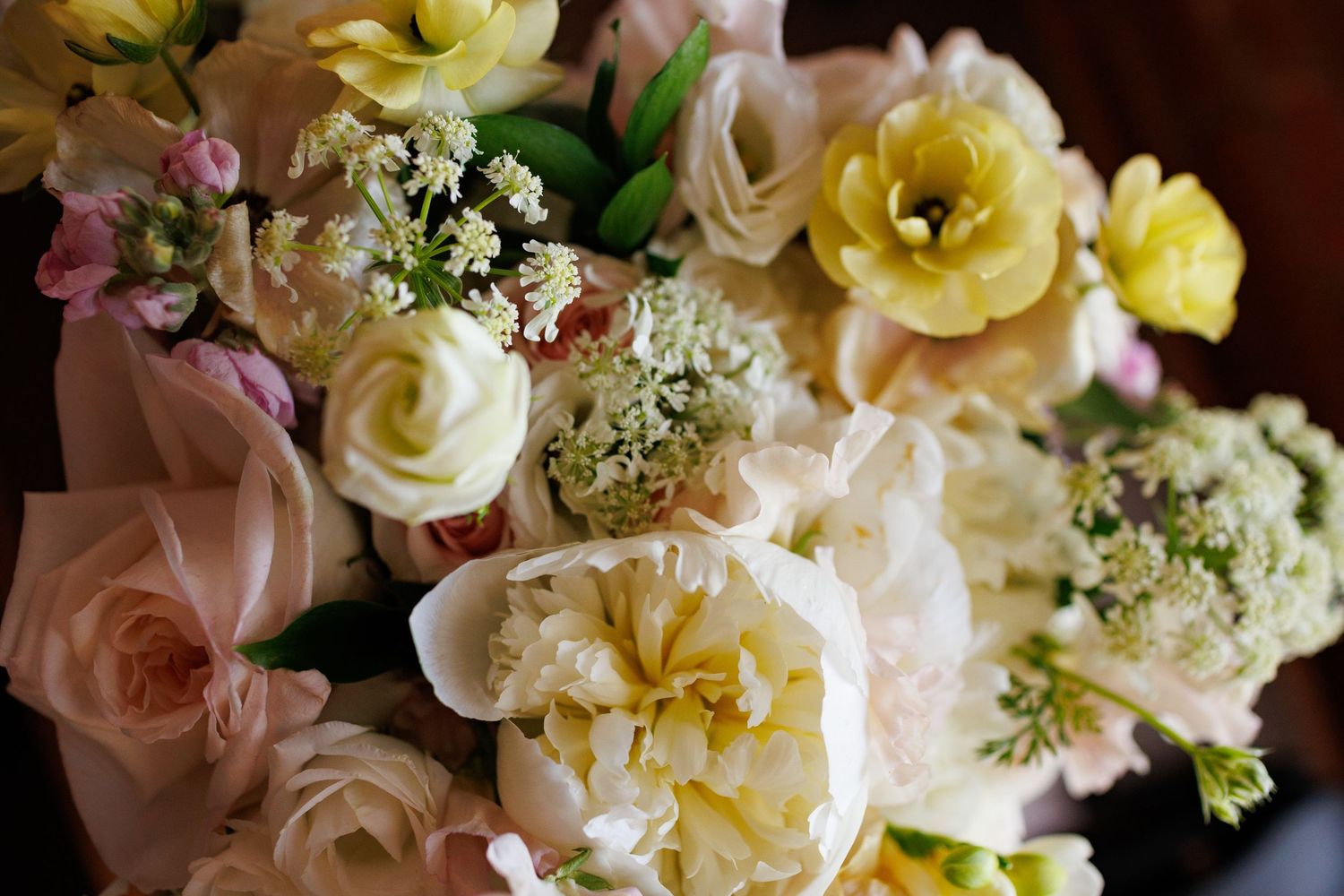 Lush wedding bouquet featuring cream peonies, yellow tulips, blush roses, and delicate white blooms arranged together.