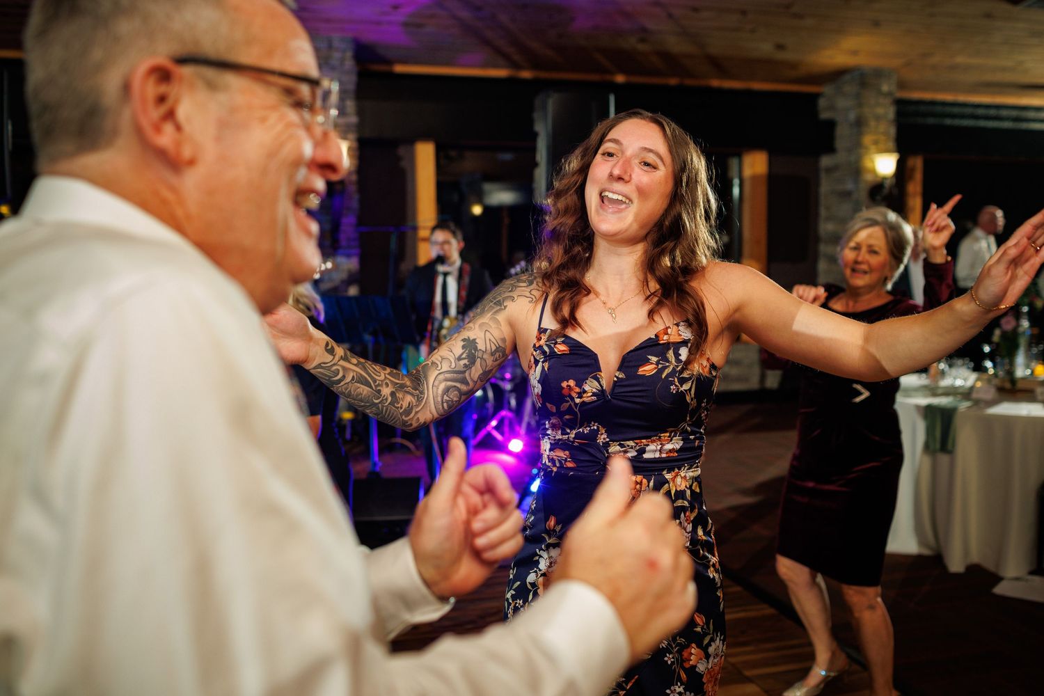 Joyful woman with tattoos laughs while dancing at a lively wedding reception.