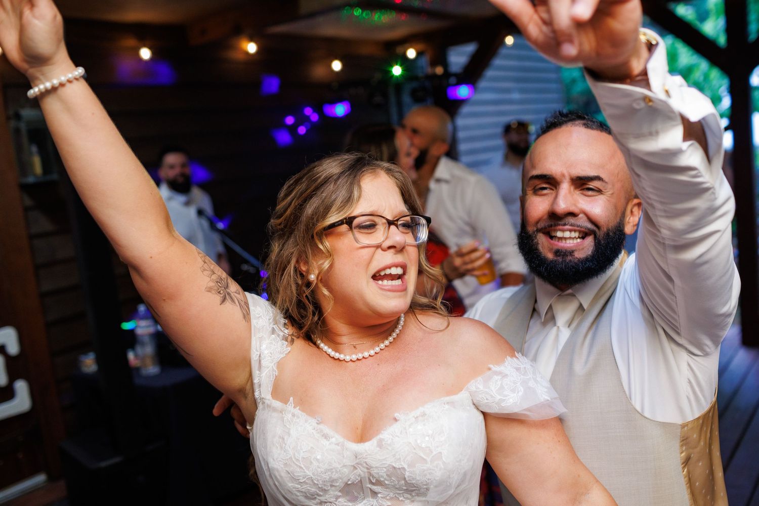 Bride and groom raise arms joyfully together on the dance floor at wedding reception.