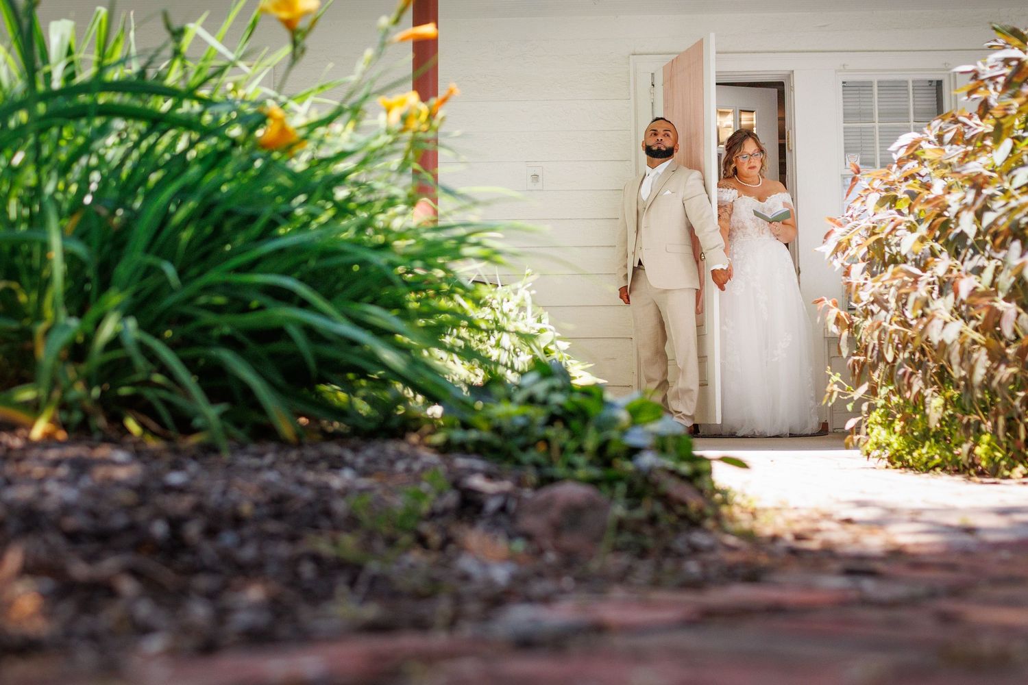 Bride and groom standing in a doorway surrounded by lush greenery on their wedding day.