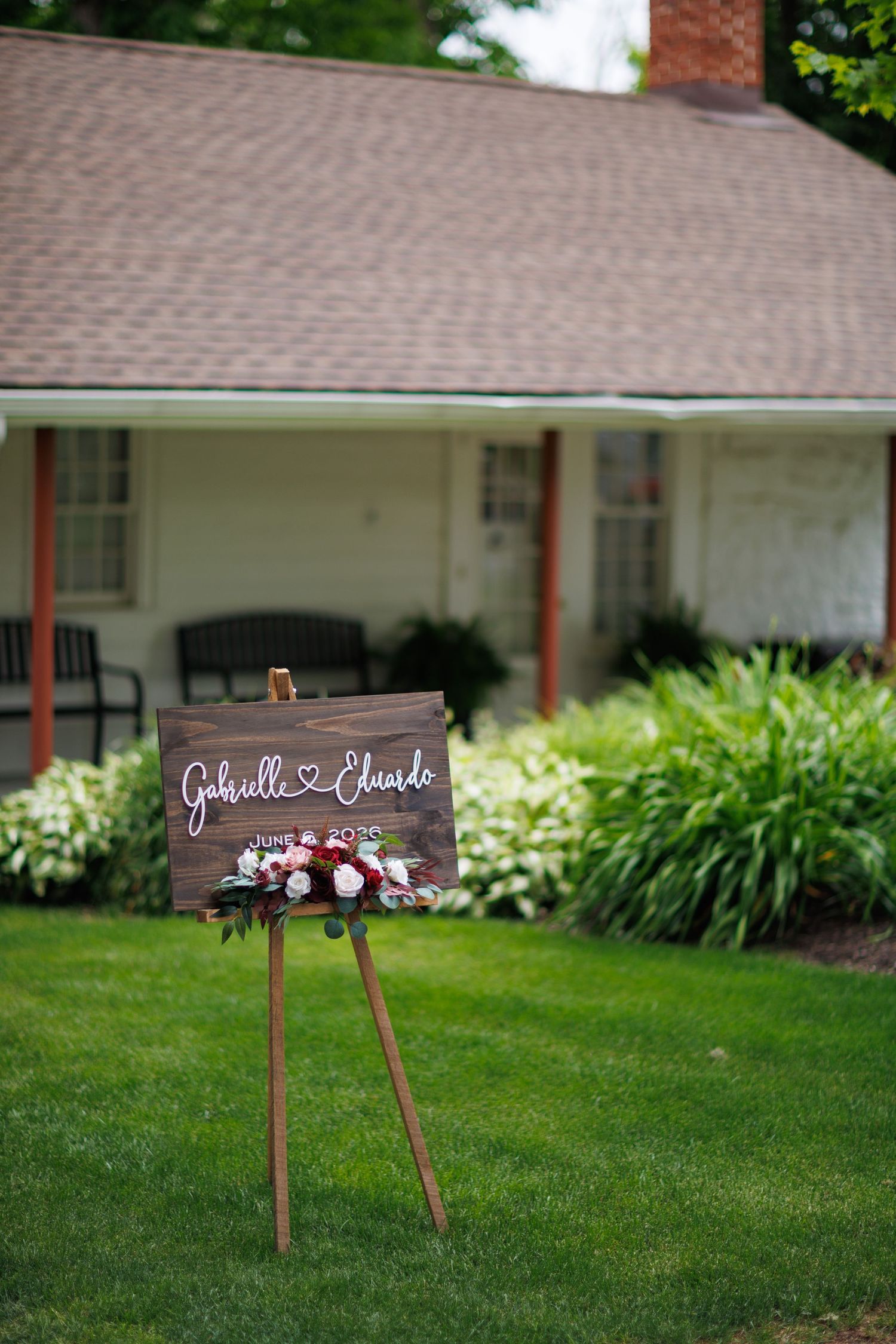 Rustic wooden wedding welcome sign for Gabrielle and Eduardo on an easel in front of a charming white house.