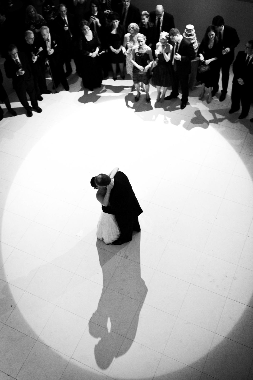 Overhead black and white view of couple dancing in spotlight surrounded by guests.