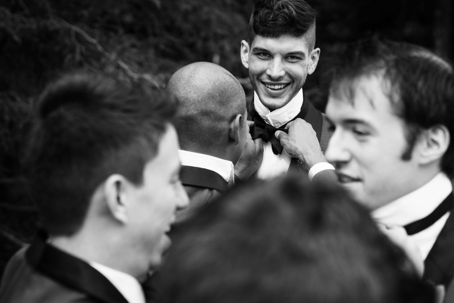 a groom laughs while a groomsman fixes his tie