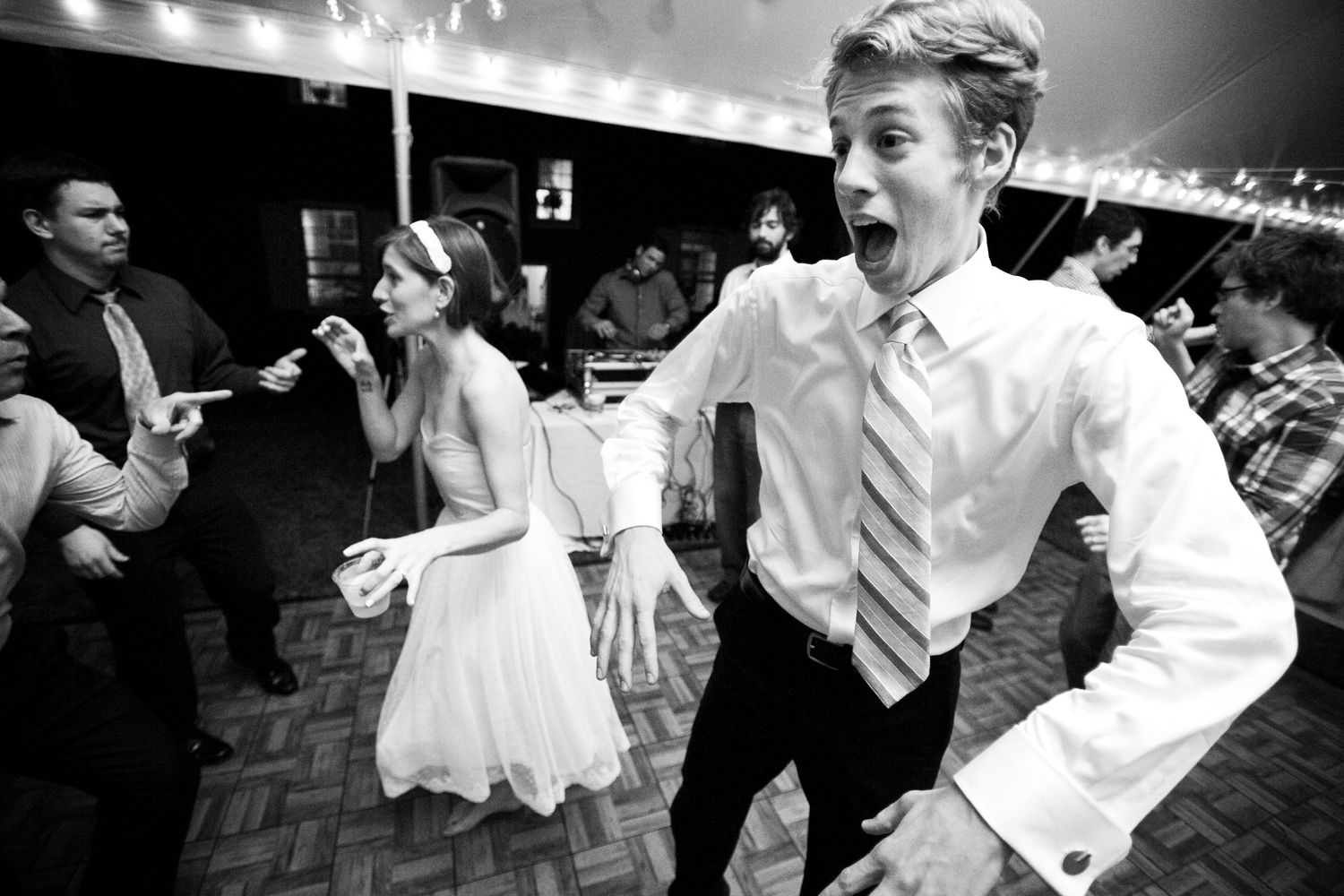 People energetically dancing at a wedding reception in black and white on a parquet floor.