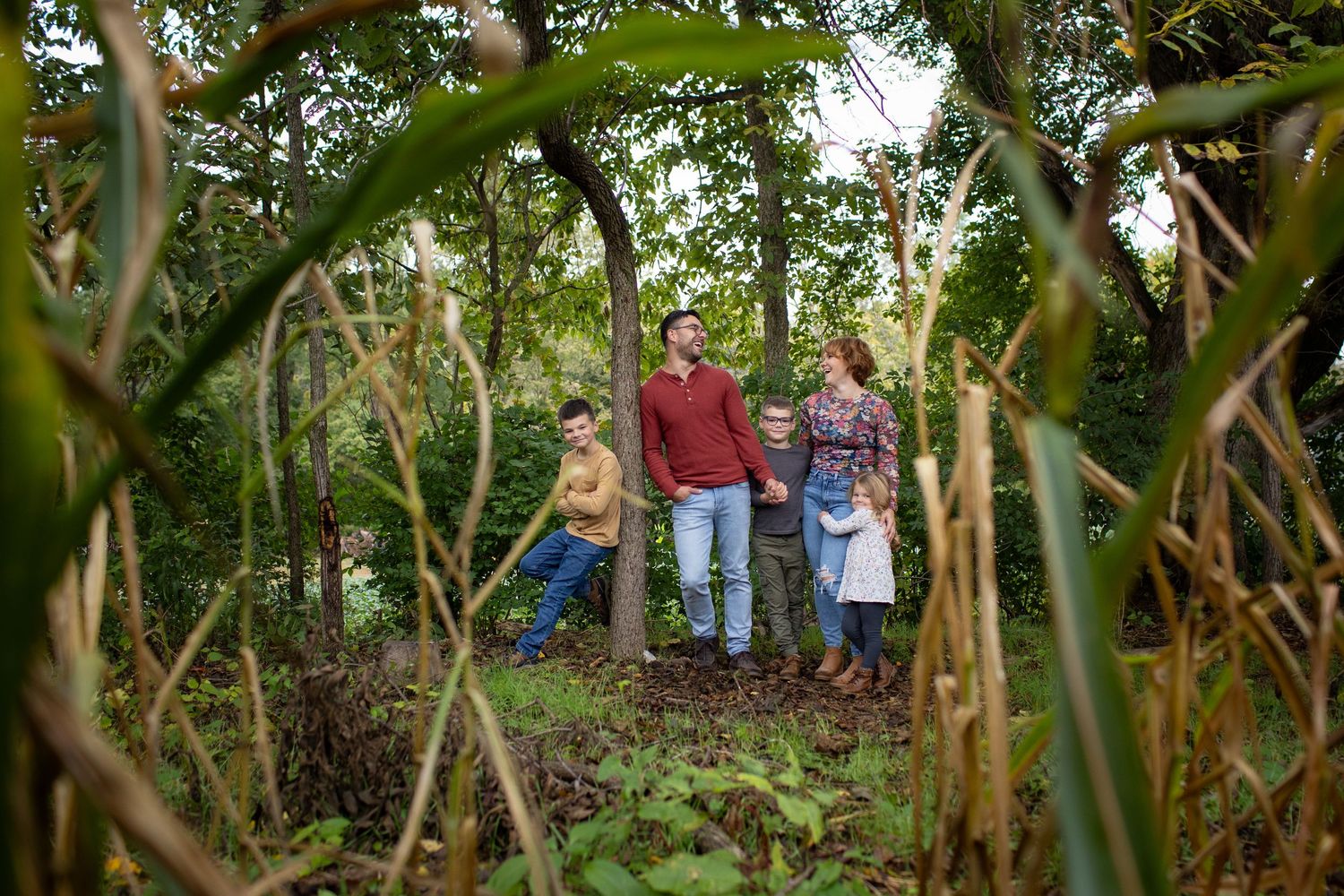 A family stands together among tall corn stalks in a rustic garden setting.