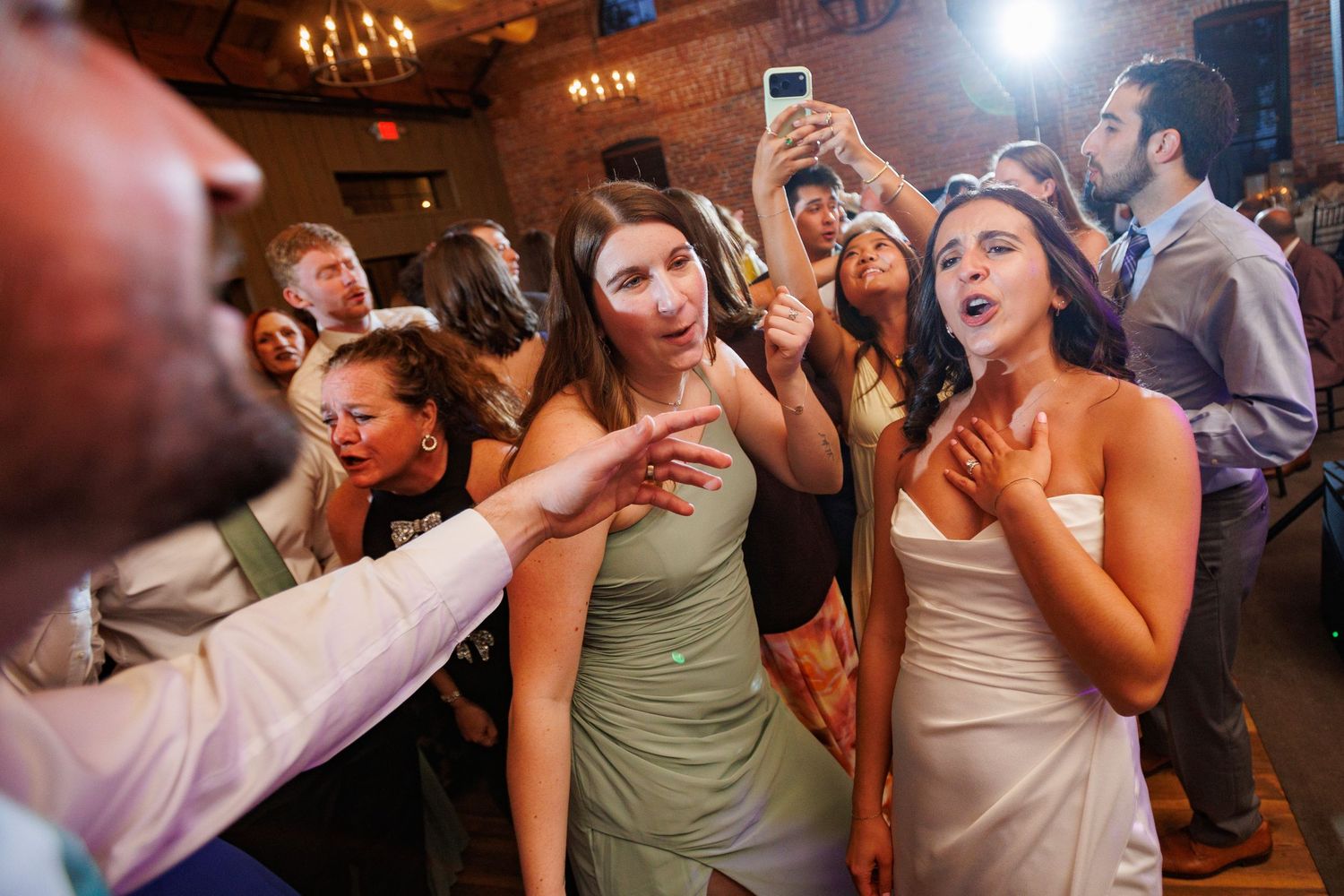 Excited wedding guests singing and dancing on crowded reception dance floor.