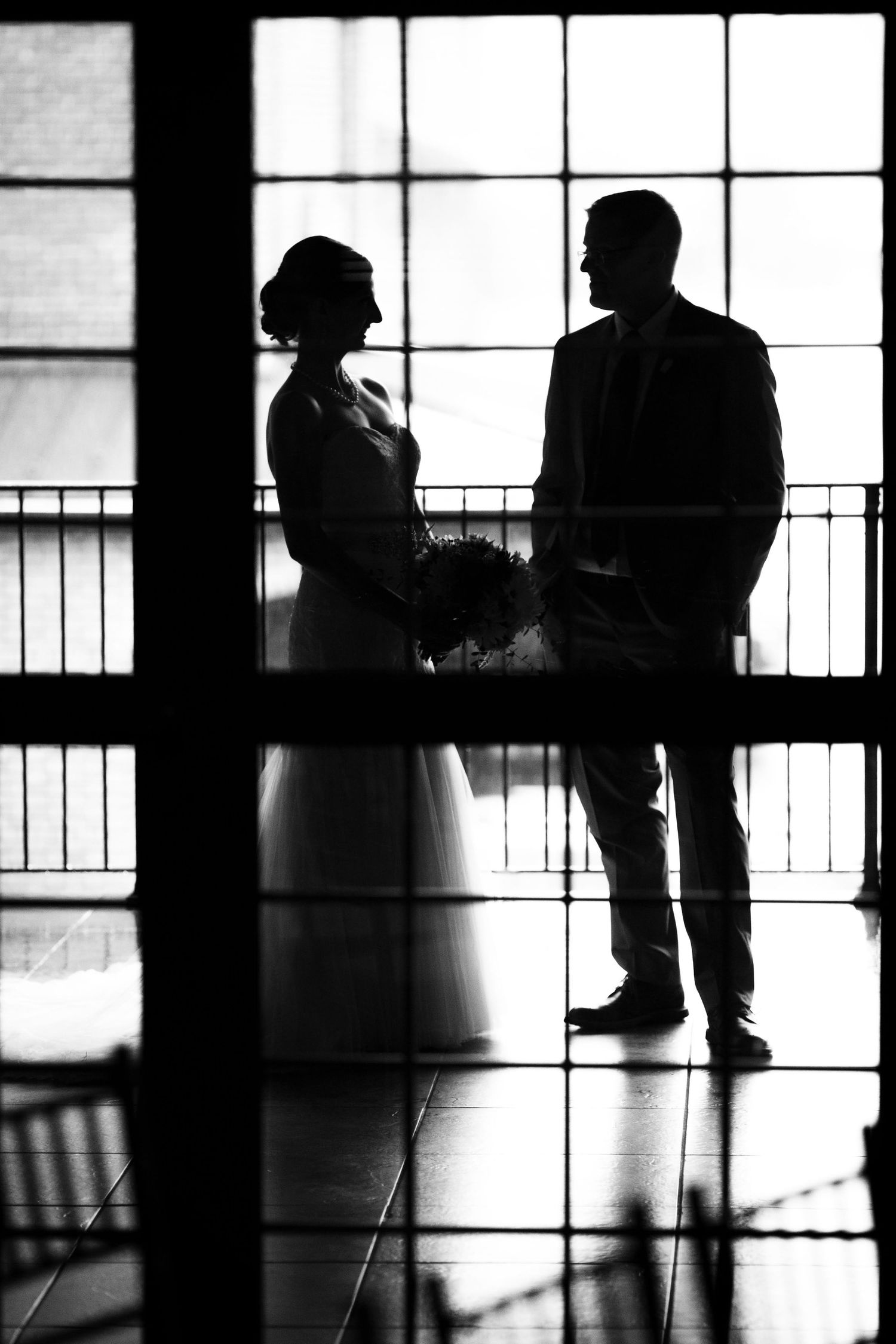 Silhouetted figures stand by a window creating a dramatic black and white wedding portrait.