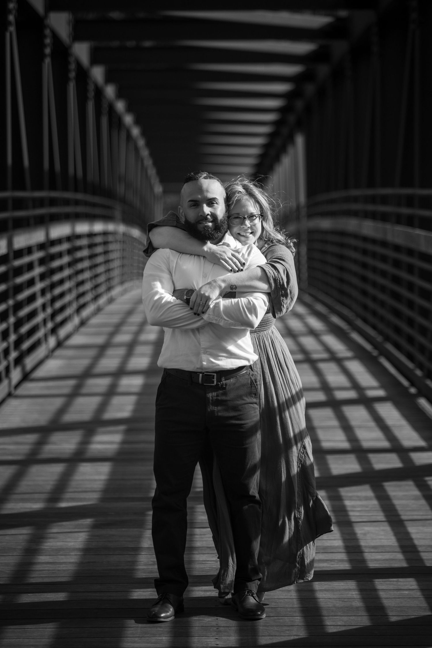 Black and white photo series showing an engaged couple dancing and embracing on a bridge with dramatic shadow patterns.