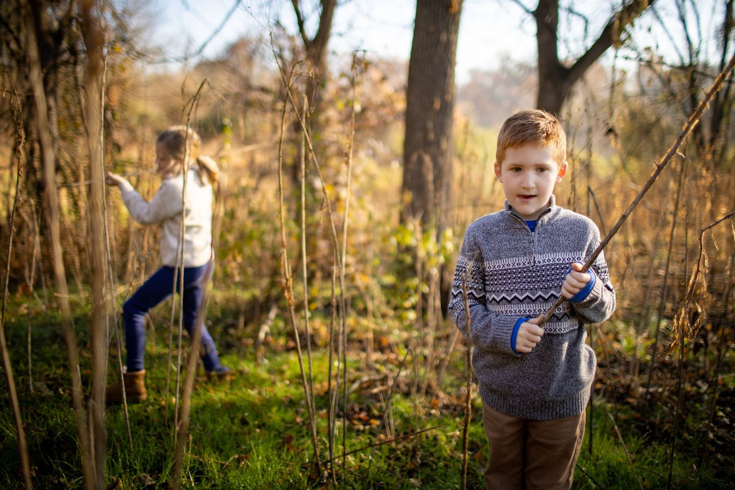 A person in a patterned sweater walks through an autumn forest path during golden hour sunlight.
