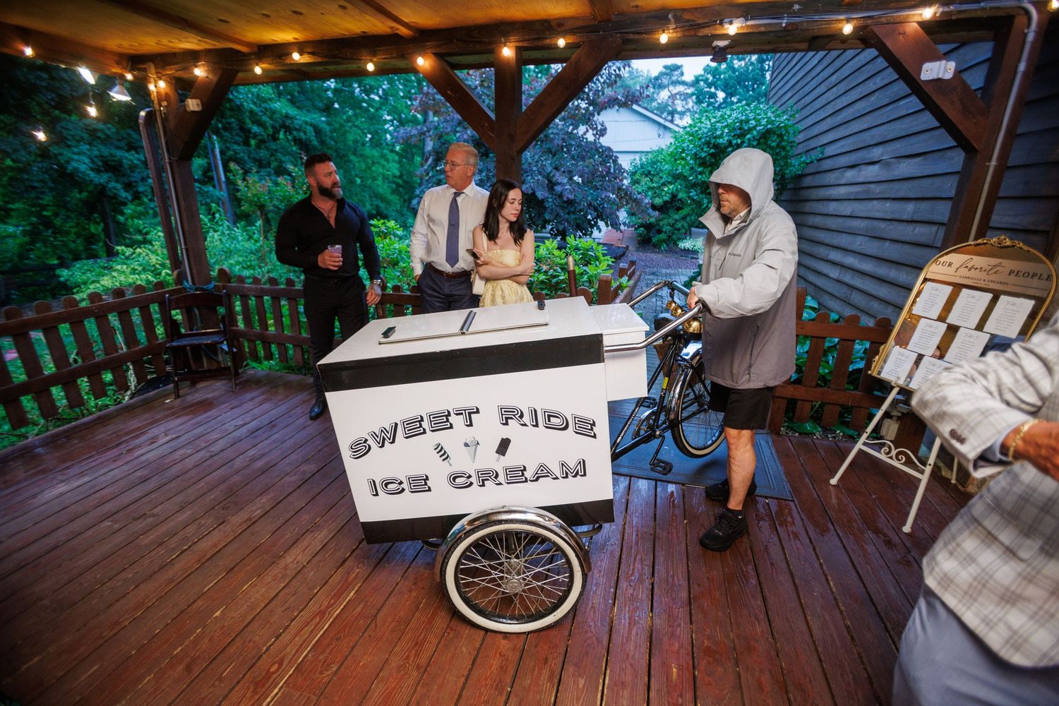 Sweet Ride Ice Cream cart on wooden deck with string lights at outdoor wedding reception at dusk.