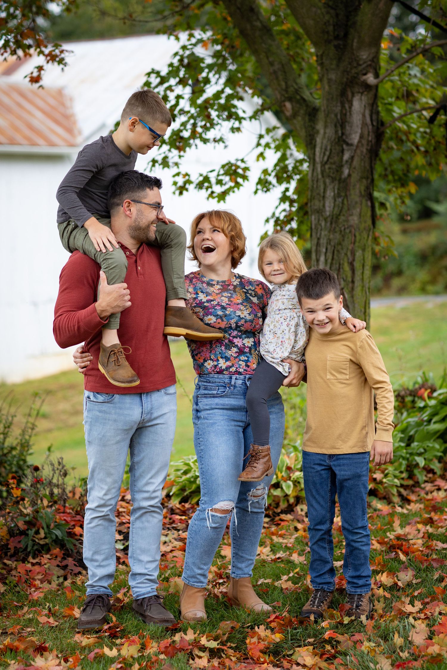 A family stands together in autumn leaves wearing casual clothing and boots.