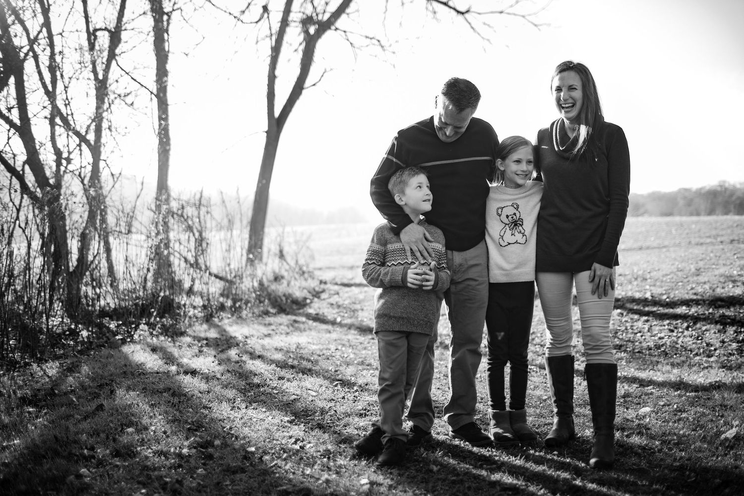 A family stands together on a sunlit path in winter, casting long shadows across the ground in black and white.