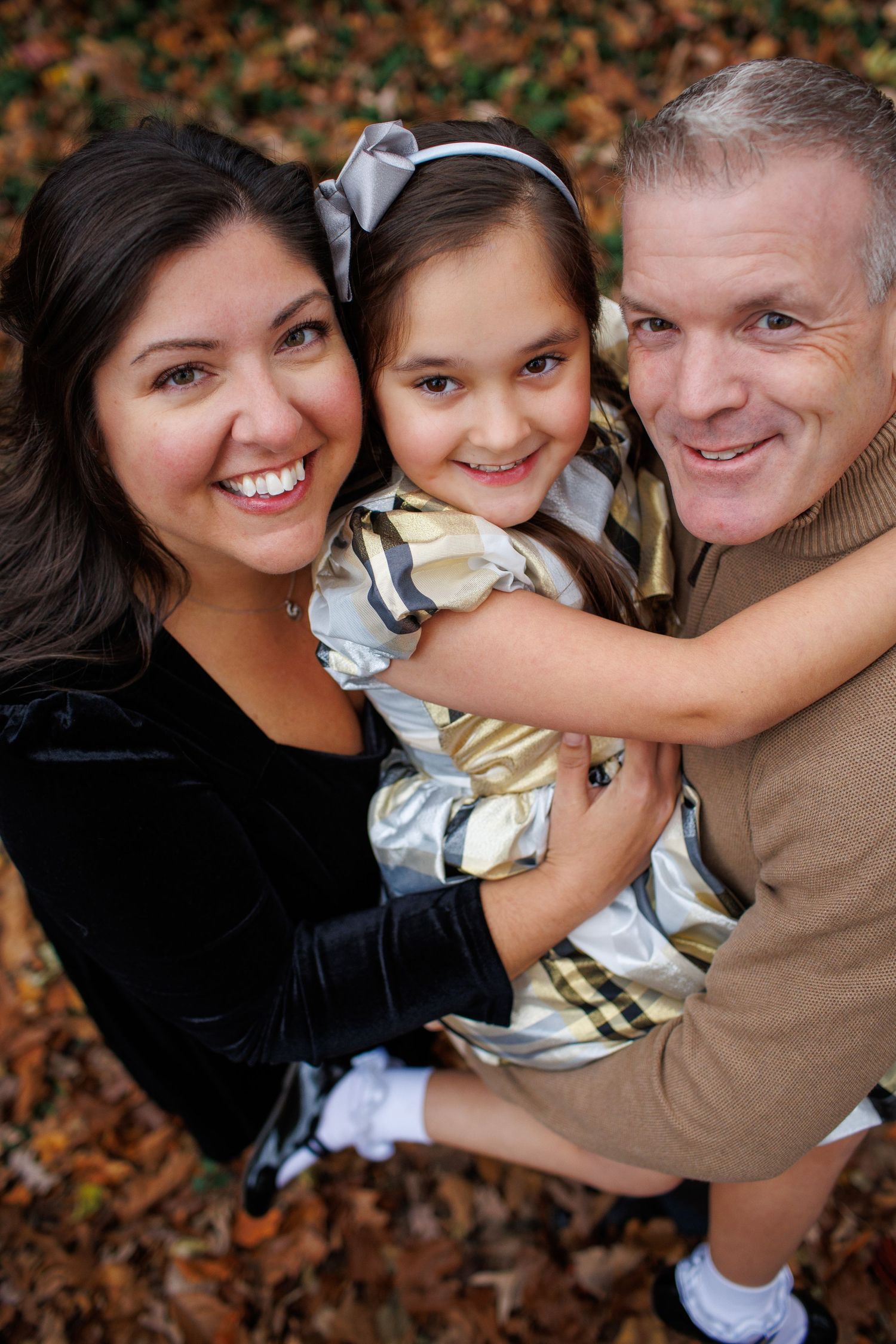 A loving family of three poses together outdoors during autumn with fallen leaves in the background.