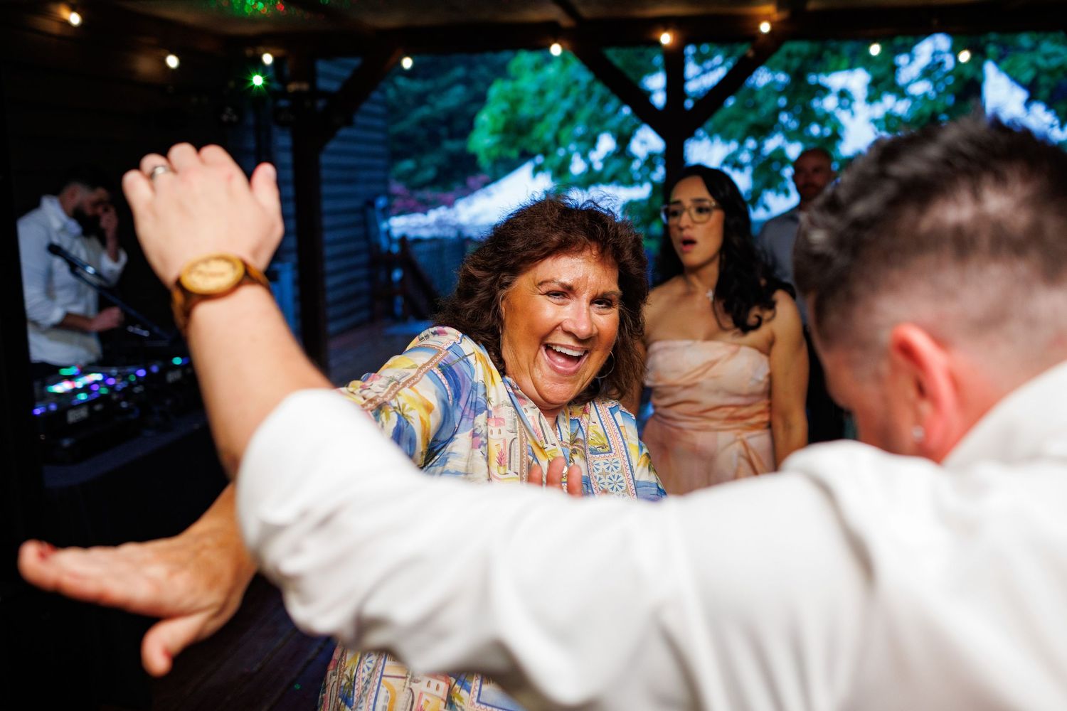 Joyful woman in colorful dress laughing and dancing with guests at lively wedding reception.