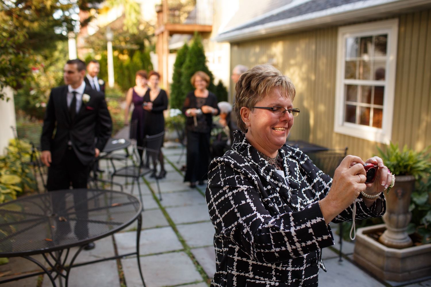 A guest in a black and white patterned shirt at an outdoor venue takes photos on their mobile device during an event.