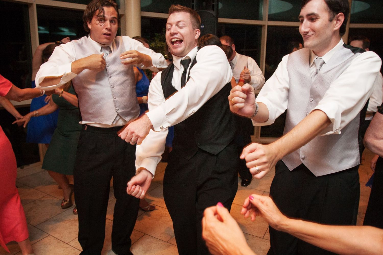 Three people in formal attire dance and laugh together at a celebration event.