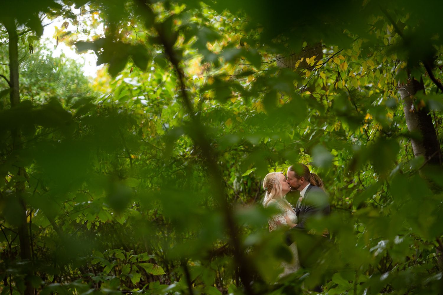 Creative wedding photo through green foliage with soft natural lighting.