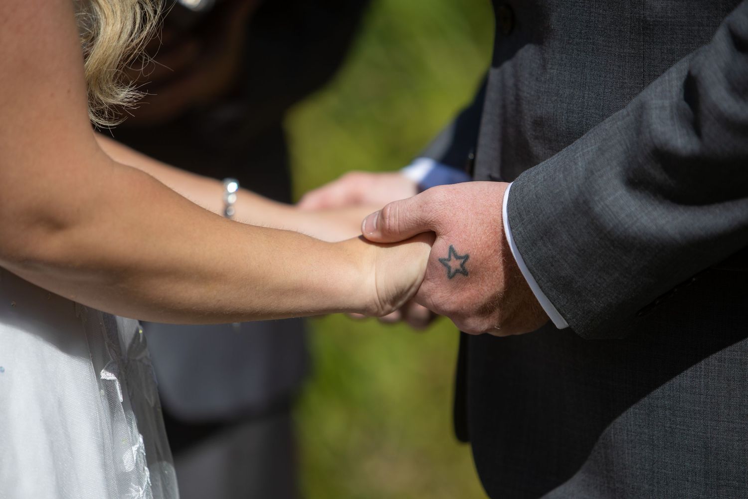 Close-up detail of hands holding during an outdoor wedding ceremony.