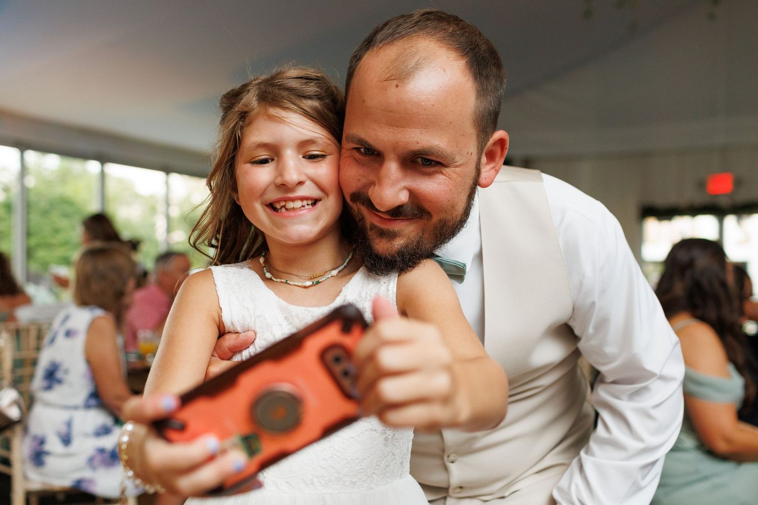 A joyful couple shares a playful moment looking at their phone during a wedding celebration.