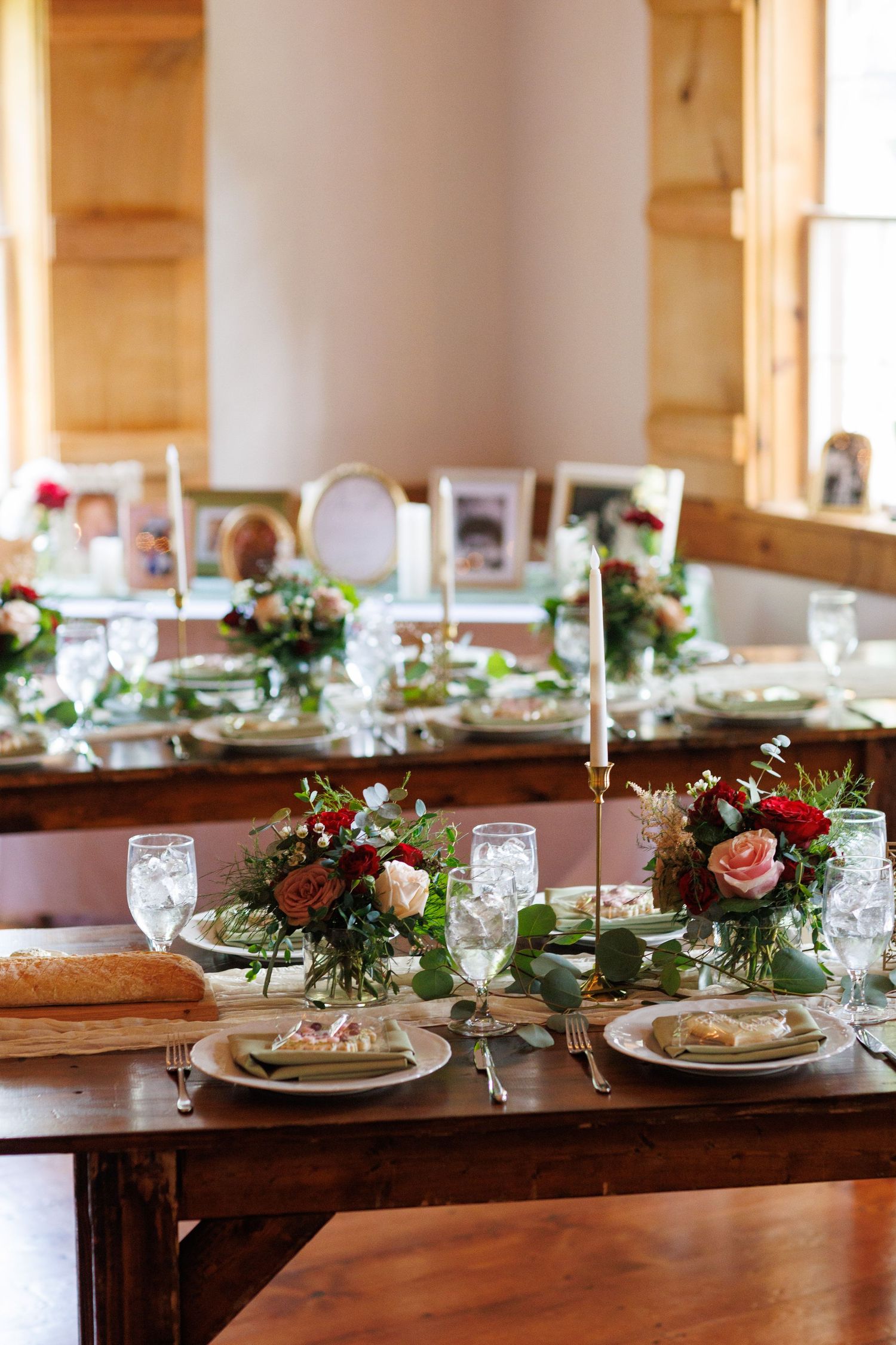Elegant rustic wedding reception table with floral centerpieces, candles, and place settings on a wooden farm table.