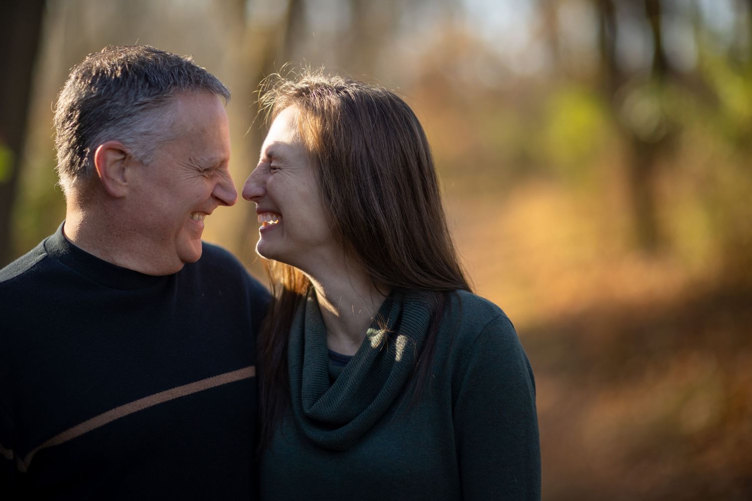 A couple shares an intimate moment while posing together in a natural outdoor setting with warm lighting.