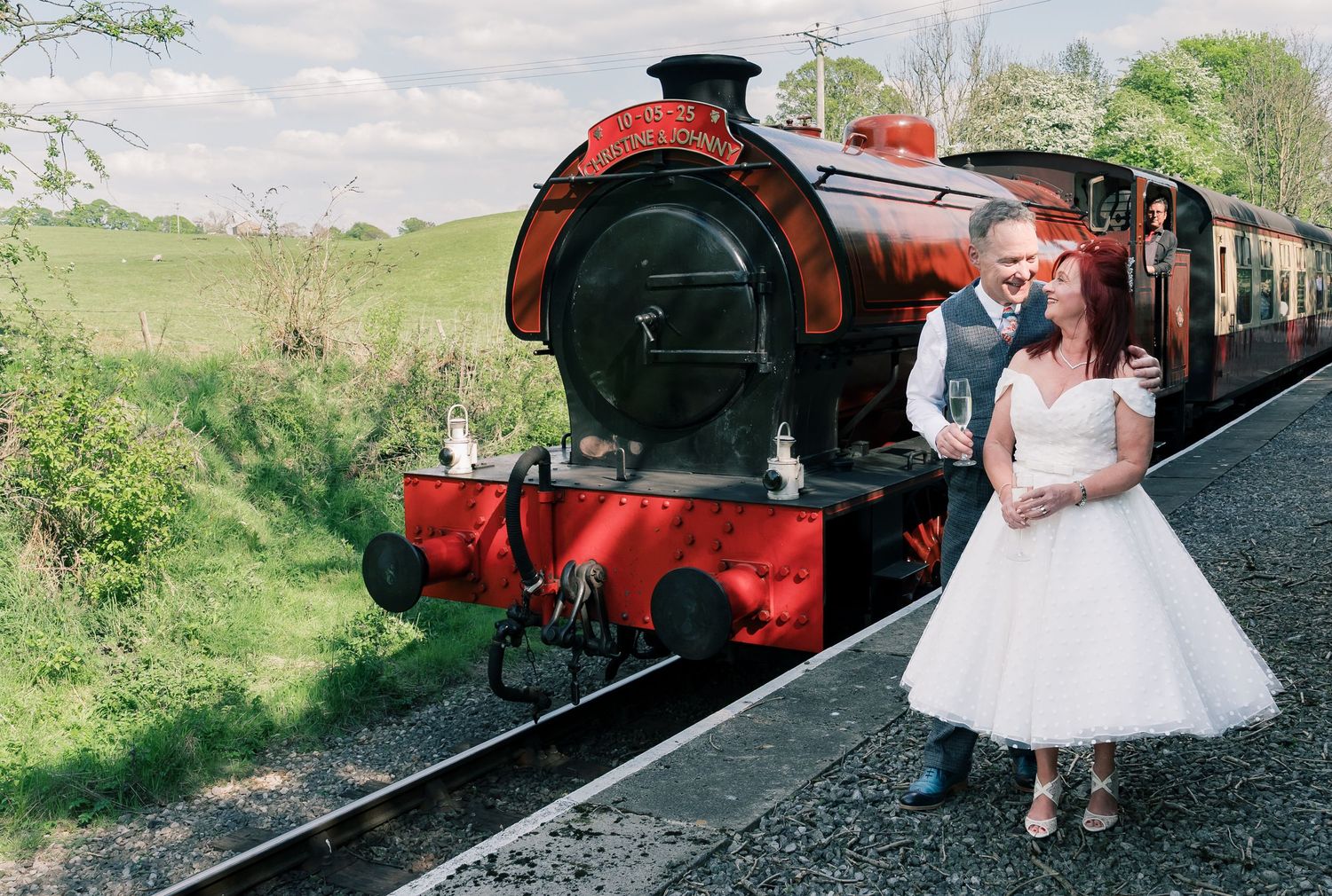 A romantic wedding photo shoot at a vintage railway station with a red steam locomotive in the background.