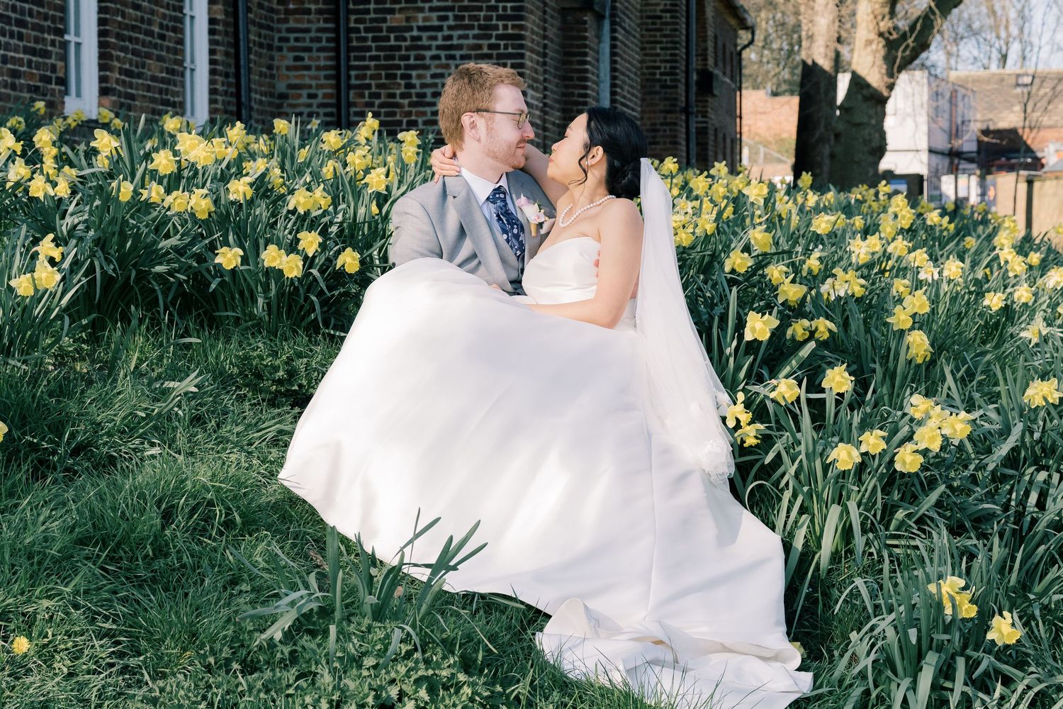 A romantic couple embraces in a spring garden filled with blooming yellow daffodils on their wedding day.