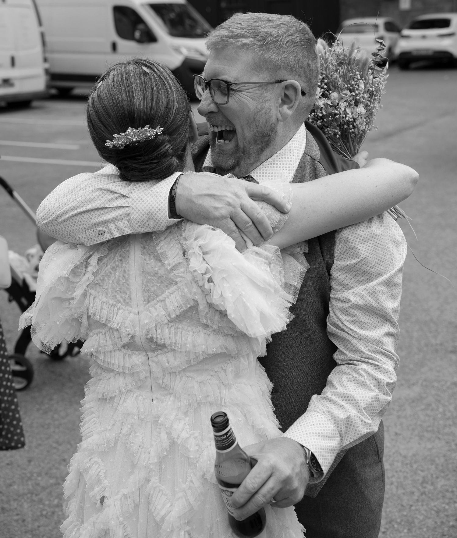 Black and white photo capturing joyful dancing and embraces at an outdoor wedding celebration.