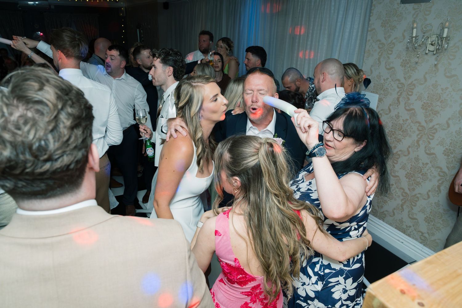 Wedding reception dance floor packed with guests celebrating under mood lighting.