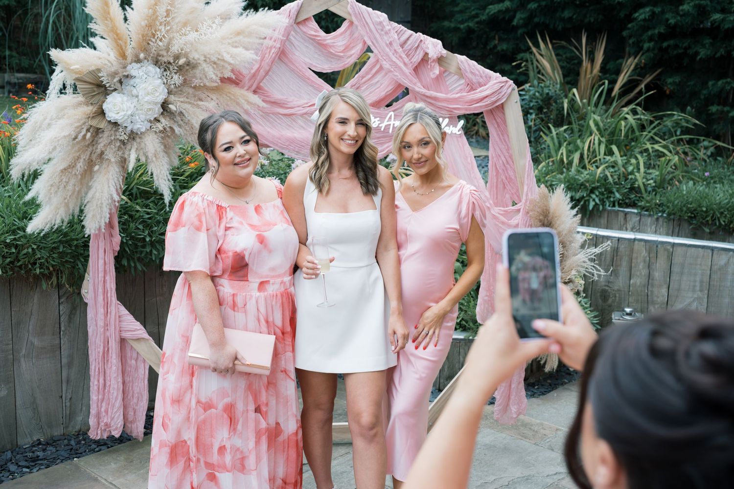 Wedding party wearing pink floral robes posing outdoors with pampas grass decorations.