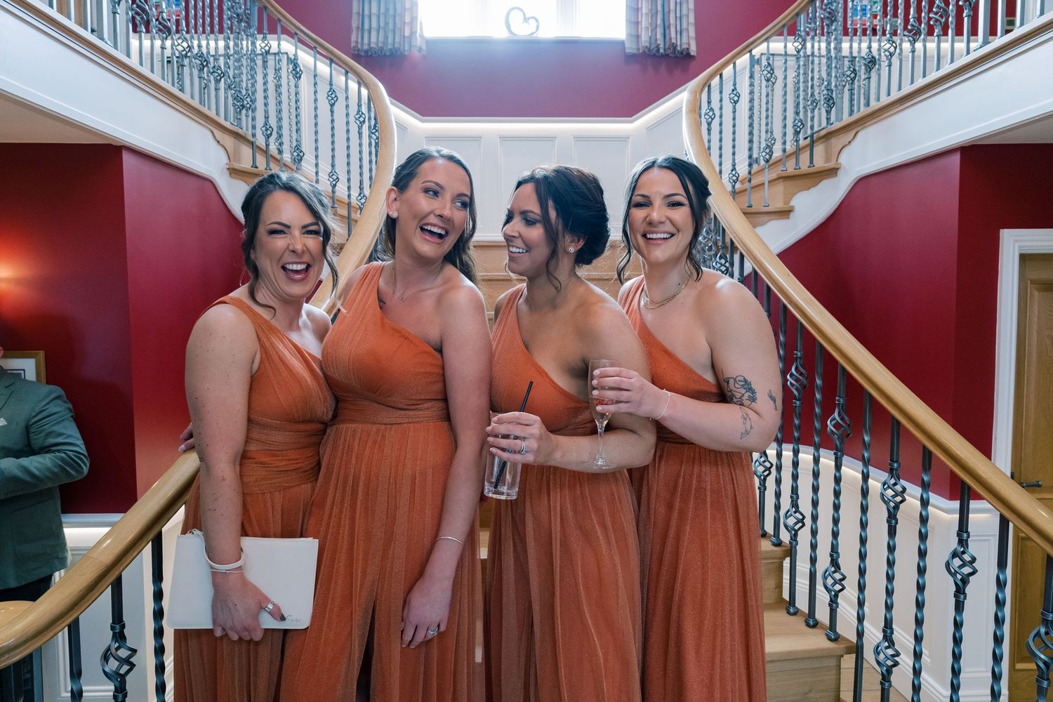 Bridesmaids in matching rust-colored dresses pose on grand staircase.