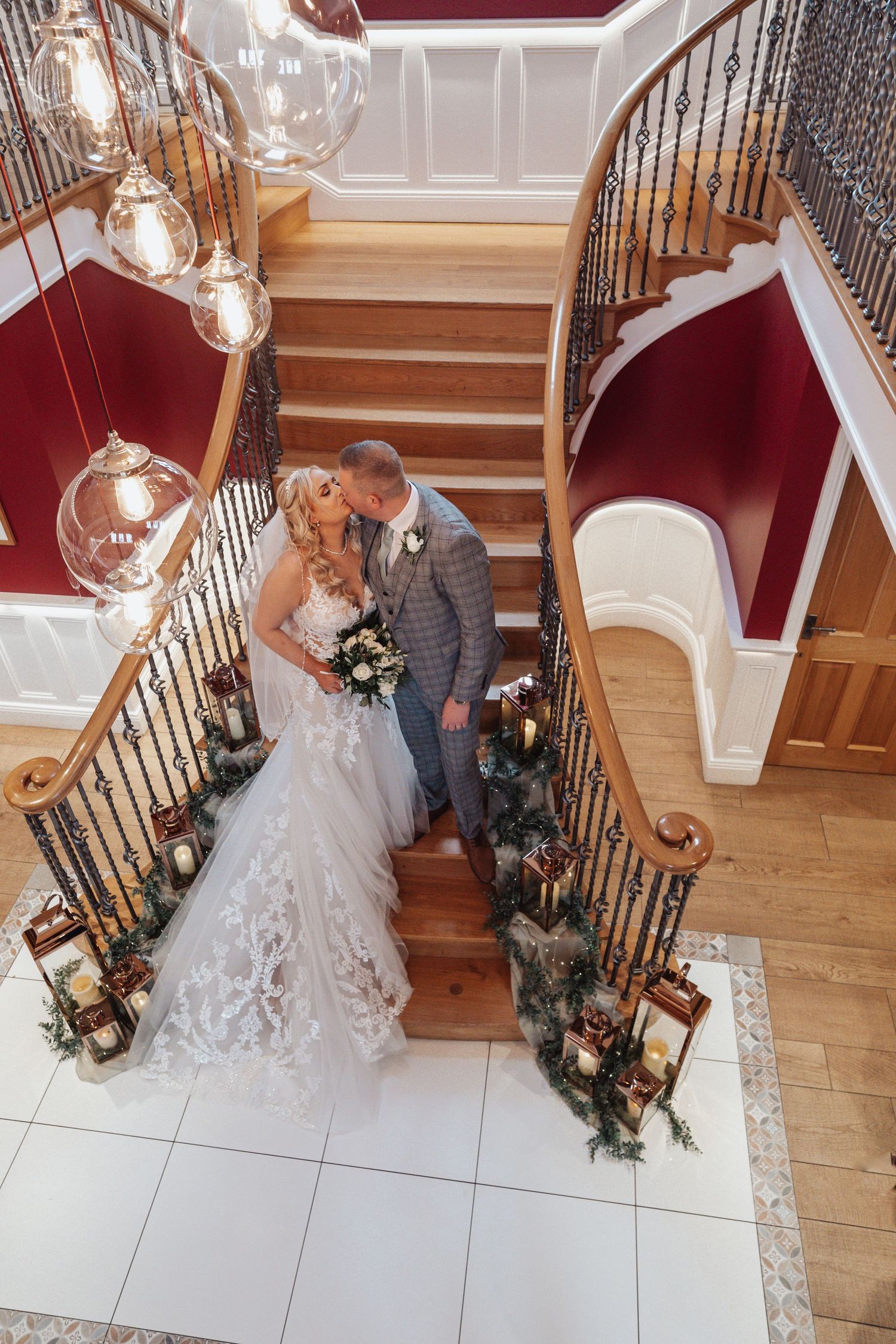 A couple embracing on a grand staircase decorated with candles and floral arrangements at their wedding.