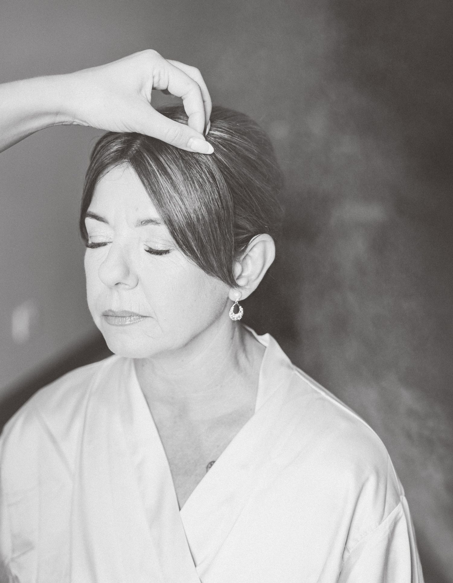 Black and white portrait of someone in a white robe with eyes closed while a hand places something in their hair.