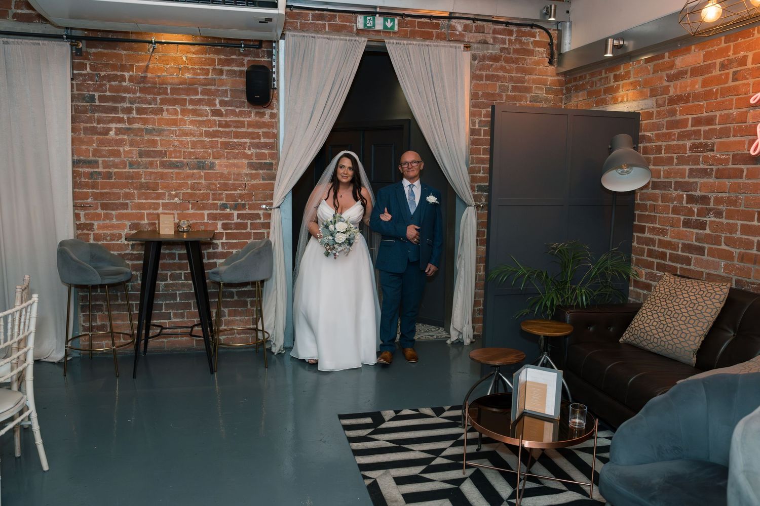 Wedding ceremony in a rustic brick-walled venue with white curtains and modern decor.