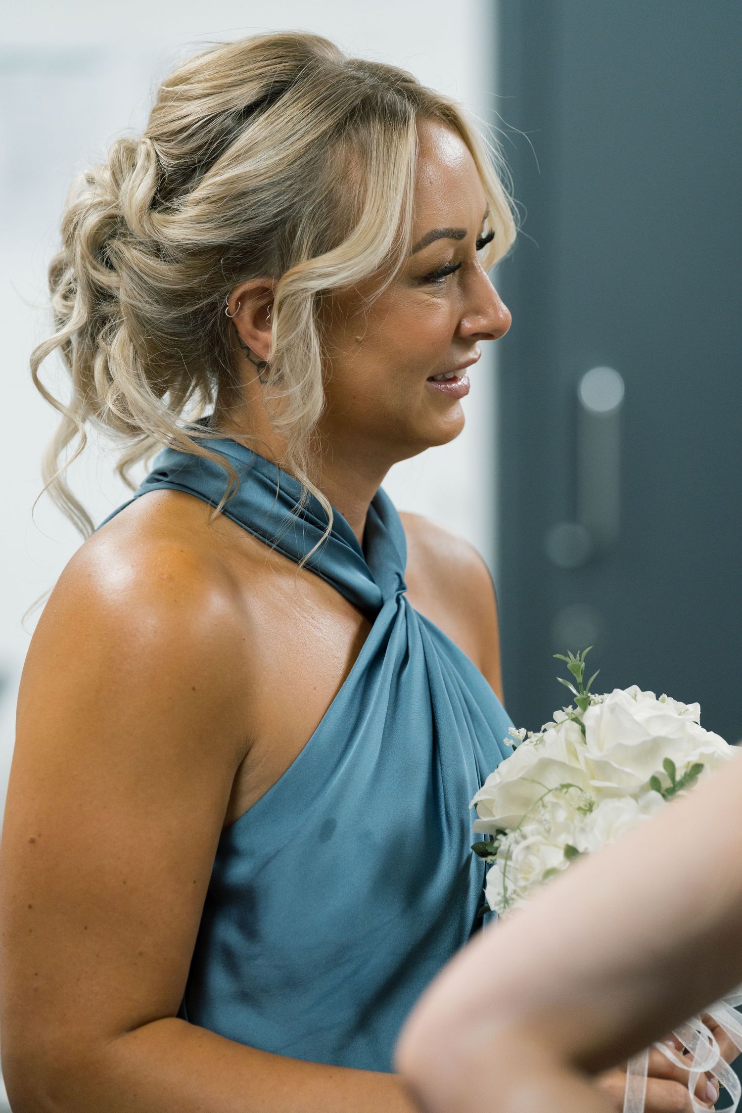 Bridesmaid in a teal halter dress holds a white floral bouquet during wedding celebrations.