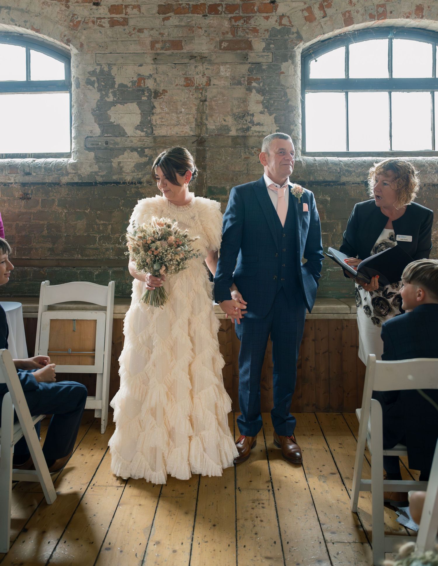Wedding ceremony in progress inside rustic brick venue with wooden floors.