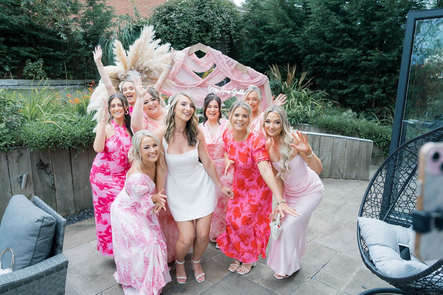 Wedding party in pink floral dresses poses together outdoors on a sunny day.