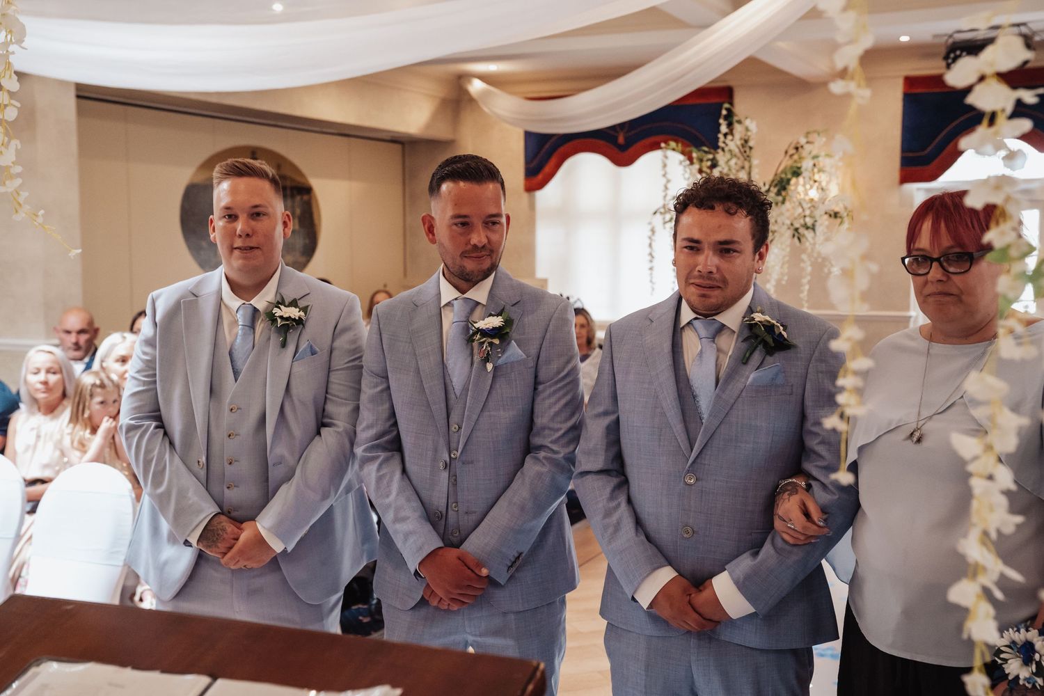 Groomsmen in matching light grey suits stand at altar during wedding ceremony.