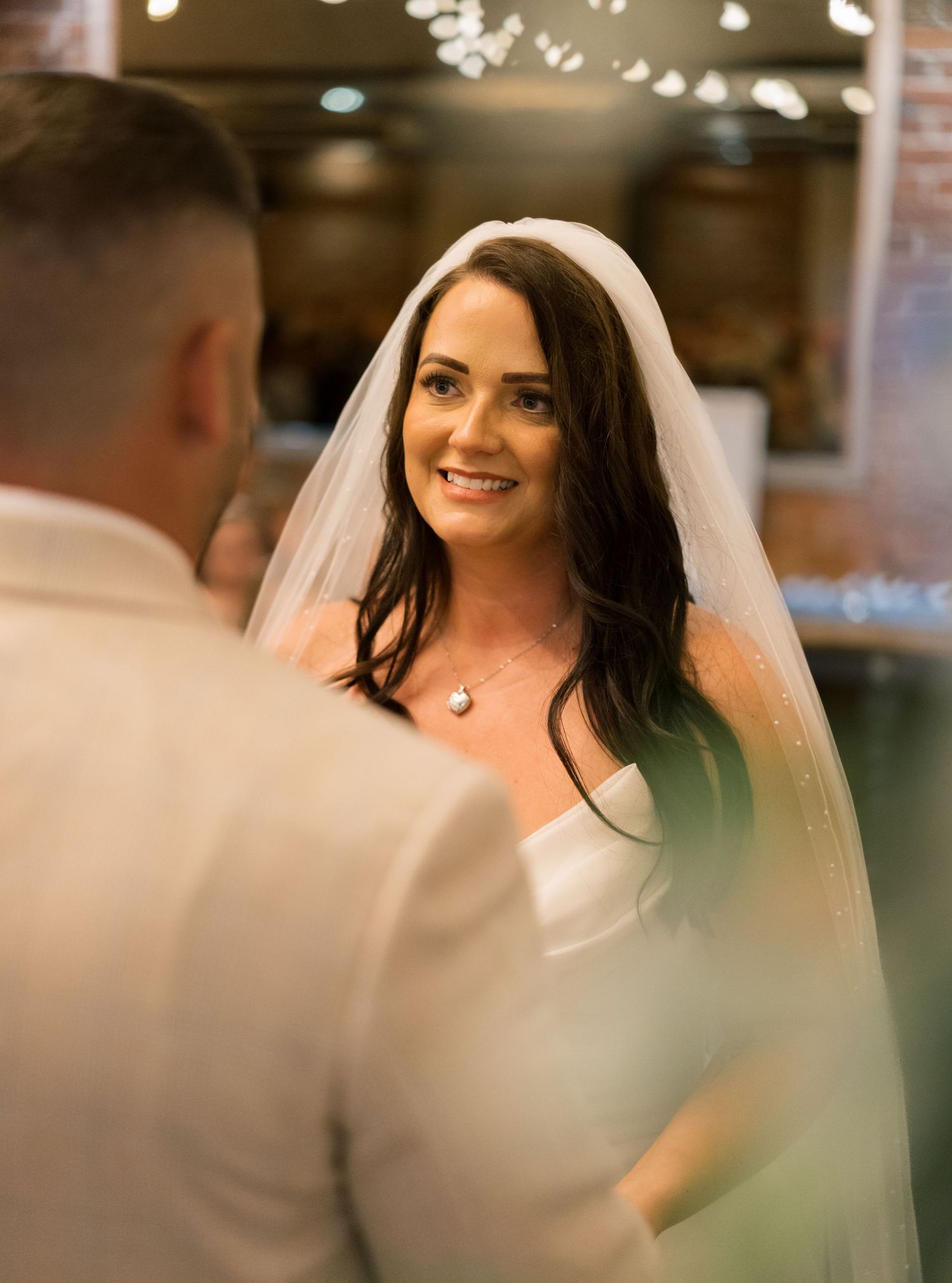 A bride in a white wedding dress and veil smiles during a candid moment at her wedding celebration at New Craven Hall, Leeds.