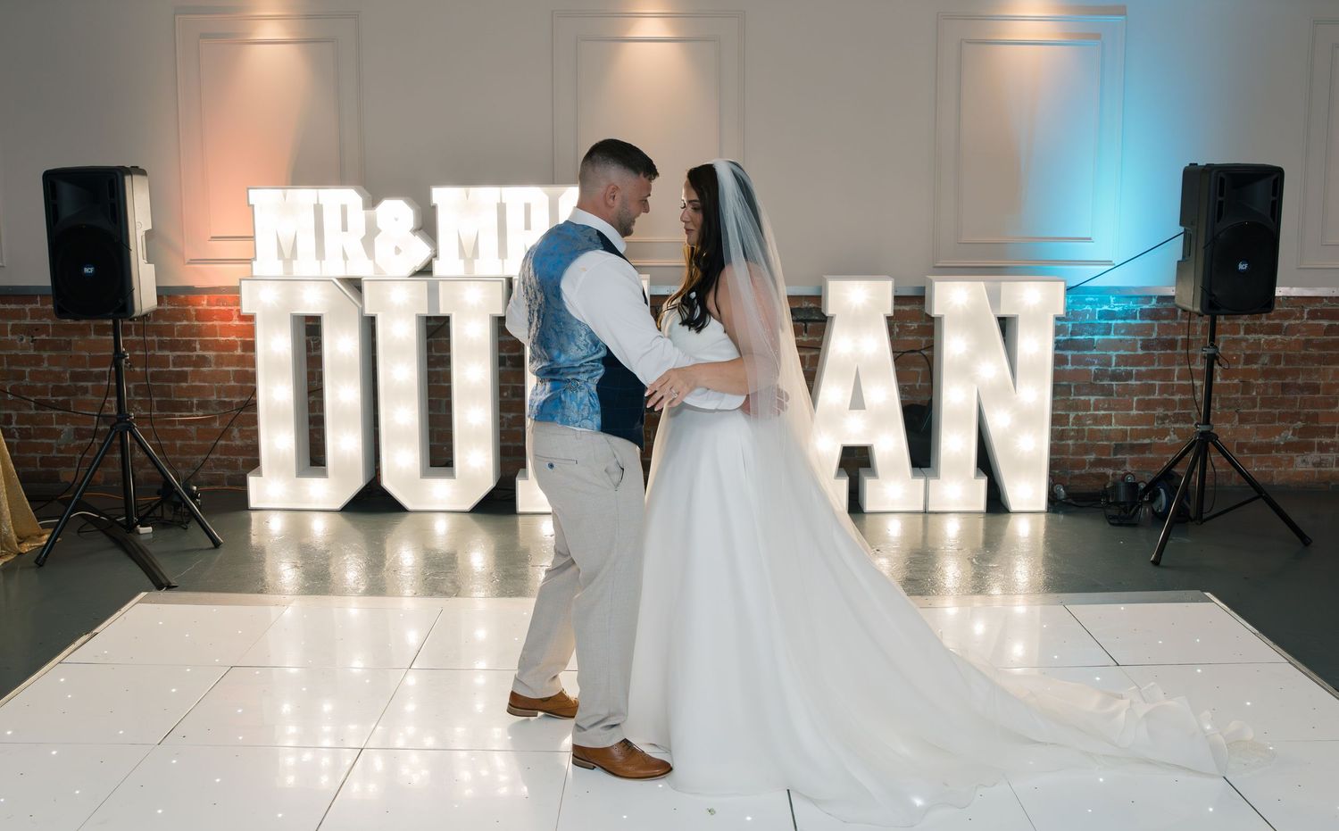 Wedding venue with illuminated marquee letters and white dance floor against exposed brick wall.