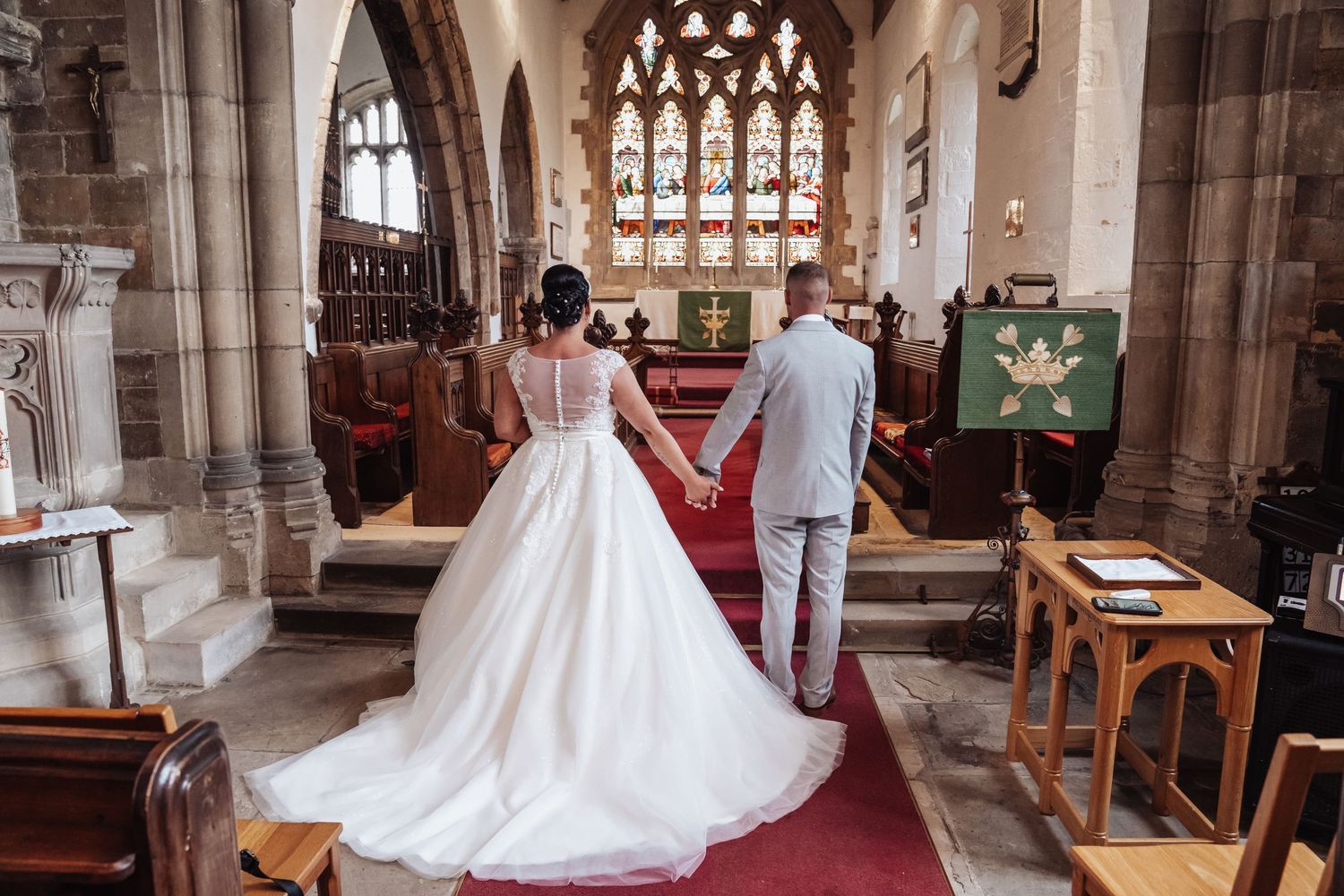 Beautiful wedding ceremony in a historic stone church with stained glass windows and red carpet aisle.