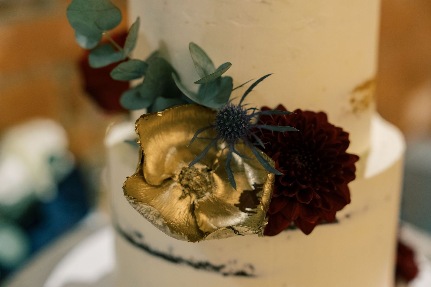 Gold and burgundy floral decoration on white wedding cake.