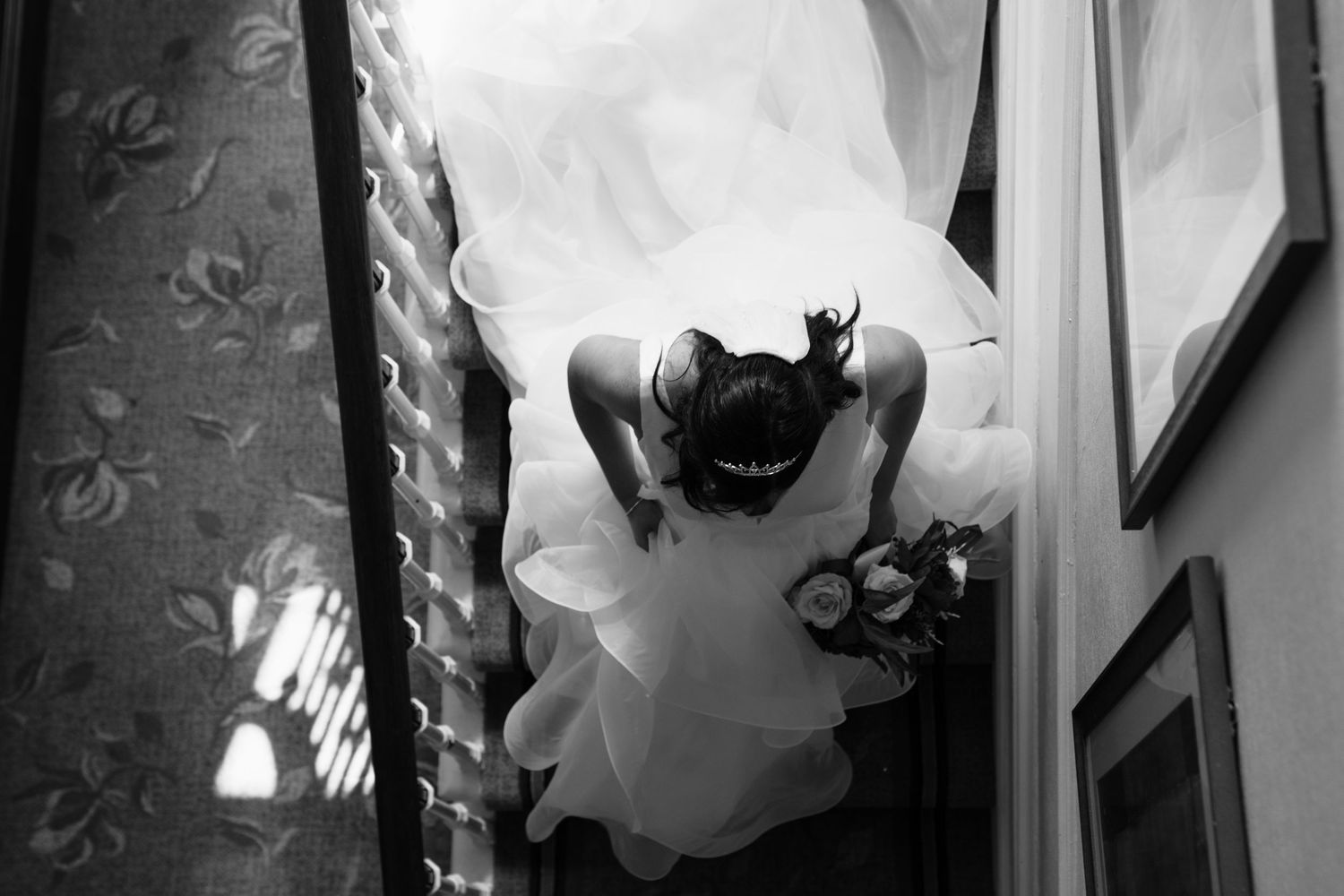 Black and white overhead view of a bride in a flowing white dress seen from above through a stairwell at Kings Croft Hotel, Pontefract.