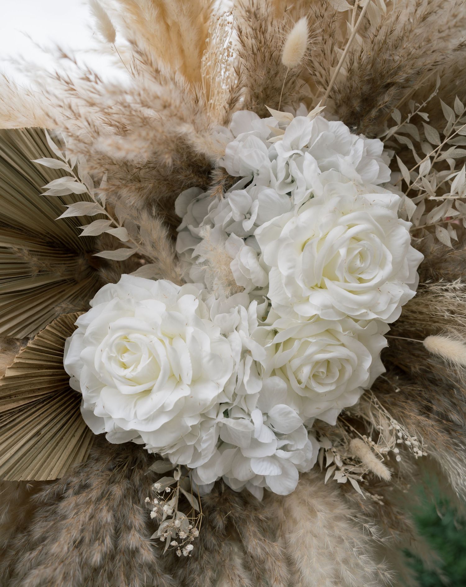 Elegant white roses arranged with dried pampas grass and palm fronds in a neutral boho wedding bouquet.