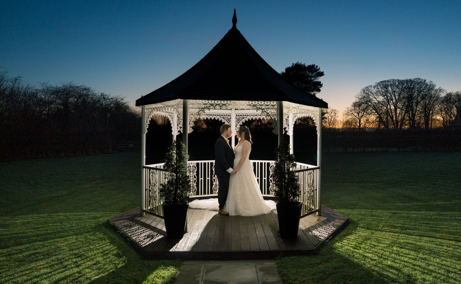 A panoramic view of a wedding gazebo at sunset with dramatic lighting and silhouettes against a darkening sky, The Bridge Hotel & SPA, Selby