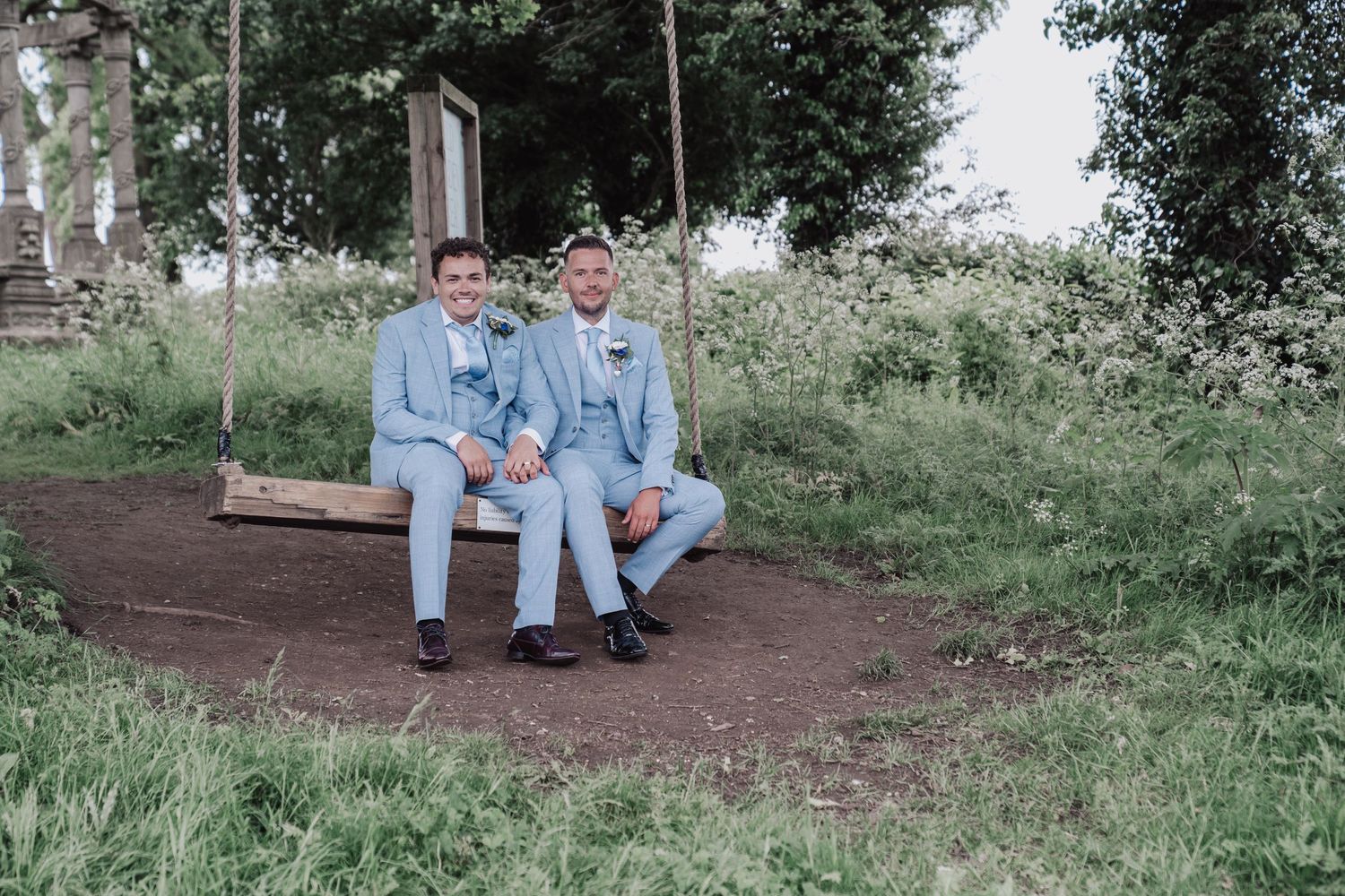 Couple in coordinating blue suits share intimate moment on garden swing surrounded by greenery.