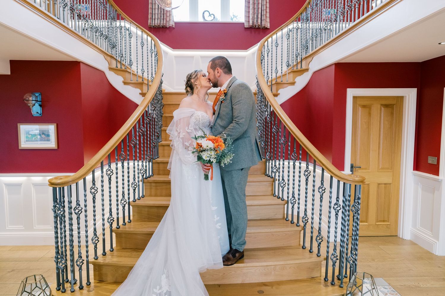 An elegant wedding photo on a grand staircase with red walls and ornate railings.