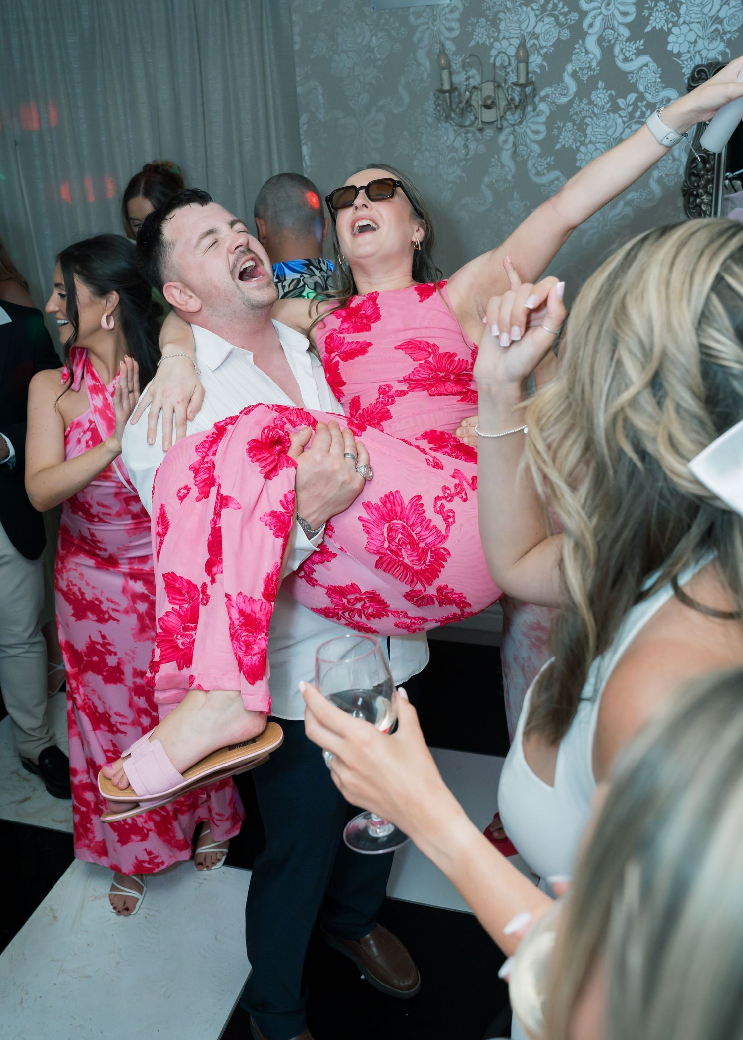 Party guests dancing and celebrating with vibrant pink outfits in a dimly lit venue.