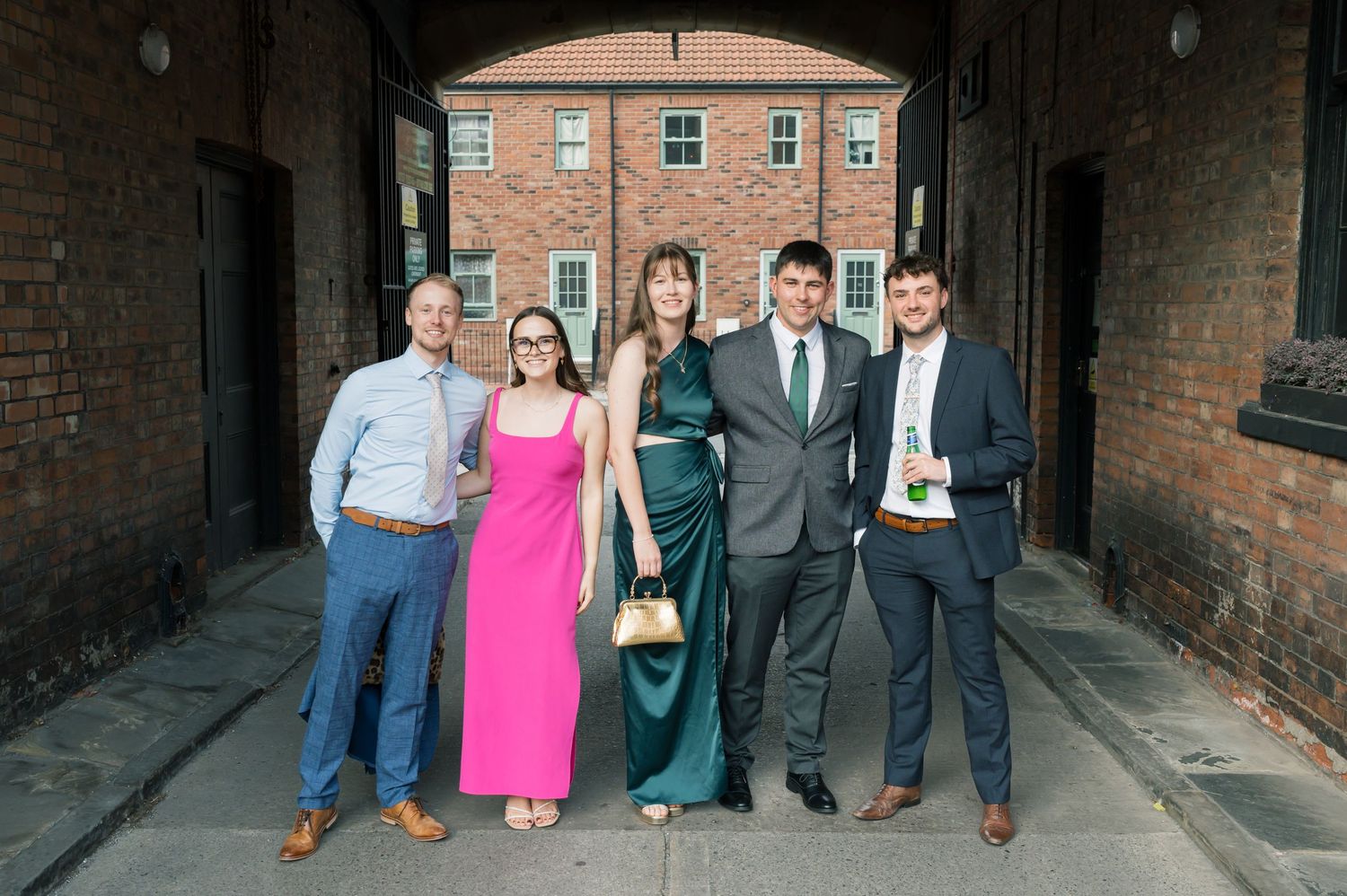 Group photo of wedding guests in formal attire standing in brick passageway.