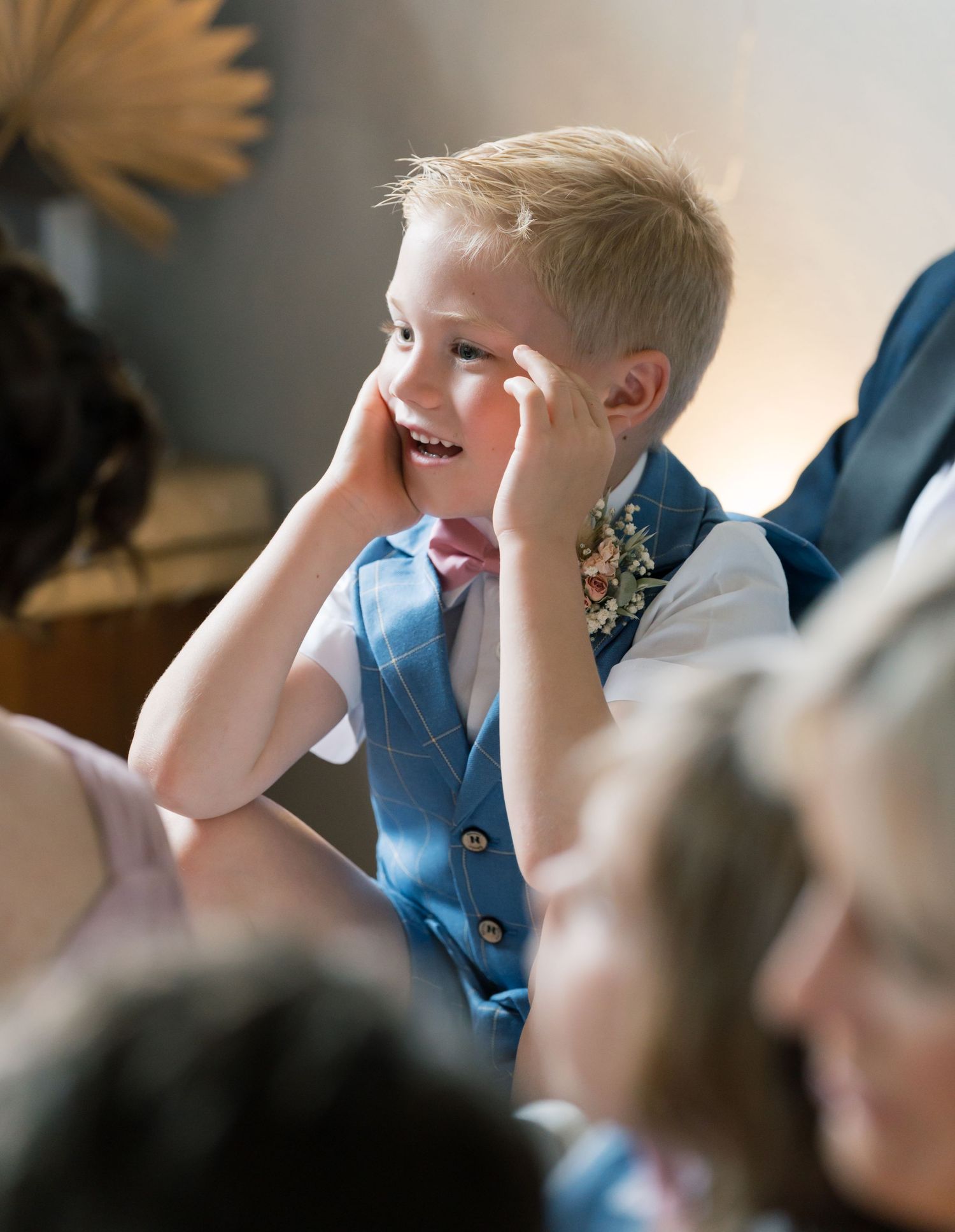 Young boy in blue suit rubs eyes during wedding ceremony.